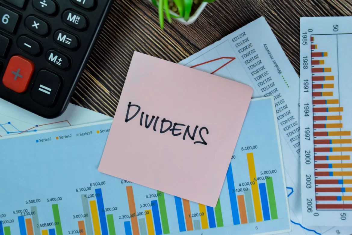 Dividends Papírek s nápisem Dividends a grafy s kalkulačkou v pozadí