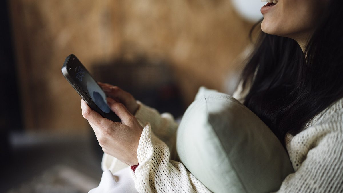 Žena s polštářem v náručí píše doma zprávu na mobilním telefonu