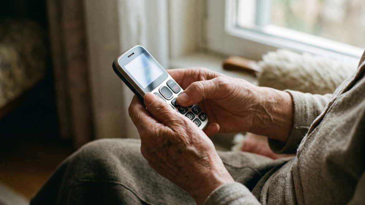 Ruce starší ženy drží mobilní telefon s velkými tlačítky